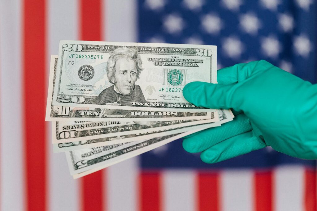 hand in medical glove holding several banknotes of American dollars in front of flag