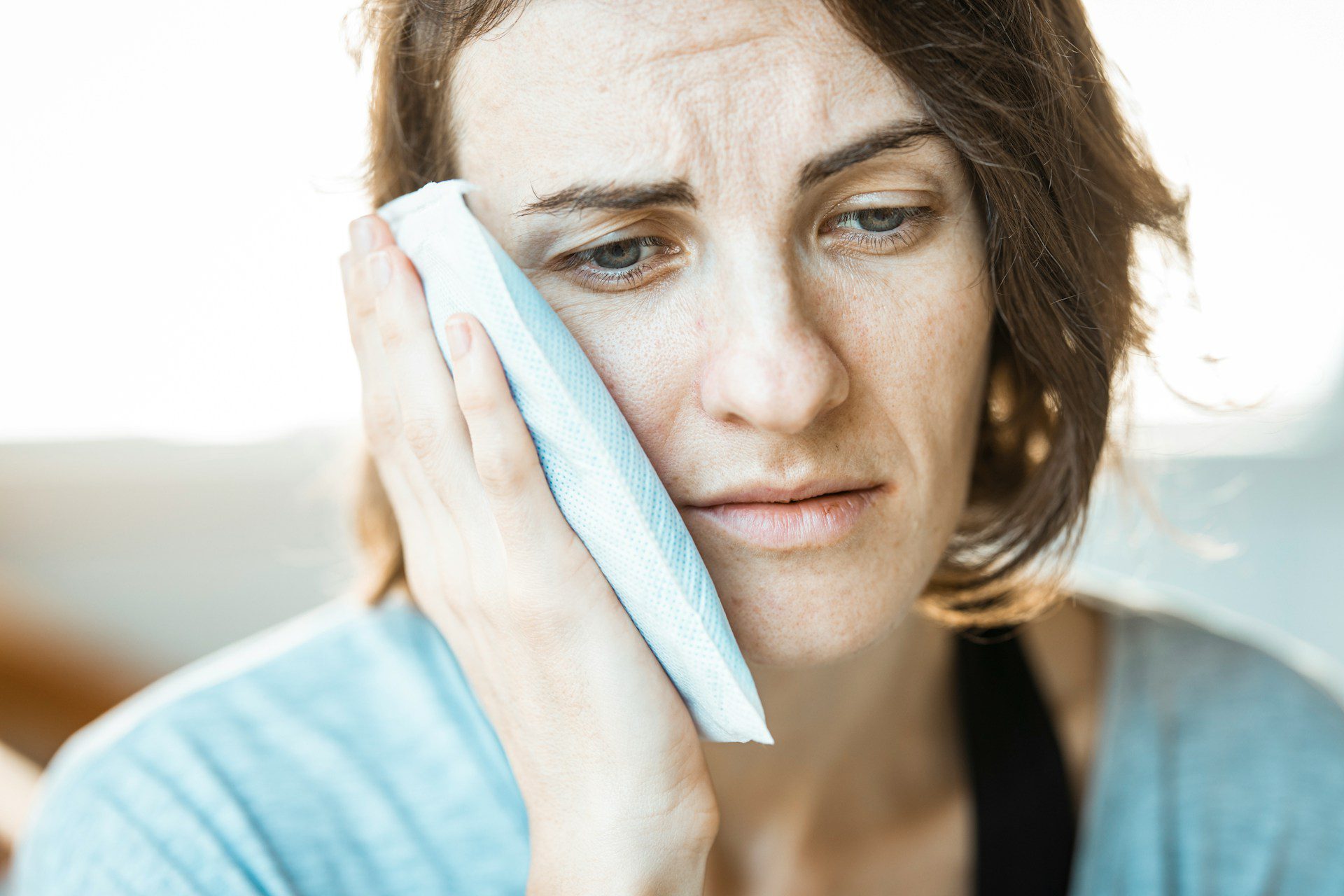 A woman in pain pressing an ice pack against her cheek