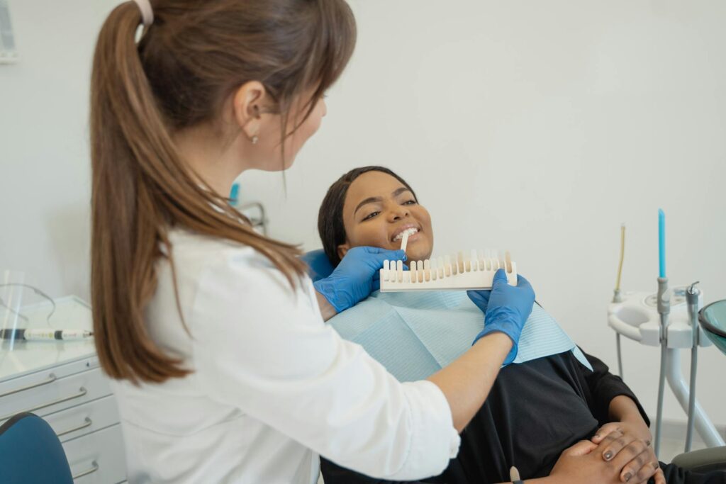 Female dentist holds tooth shade guide to patient’s mouth